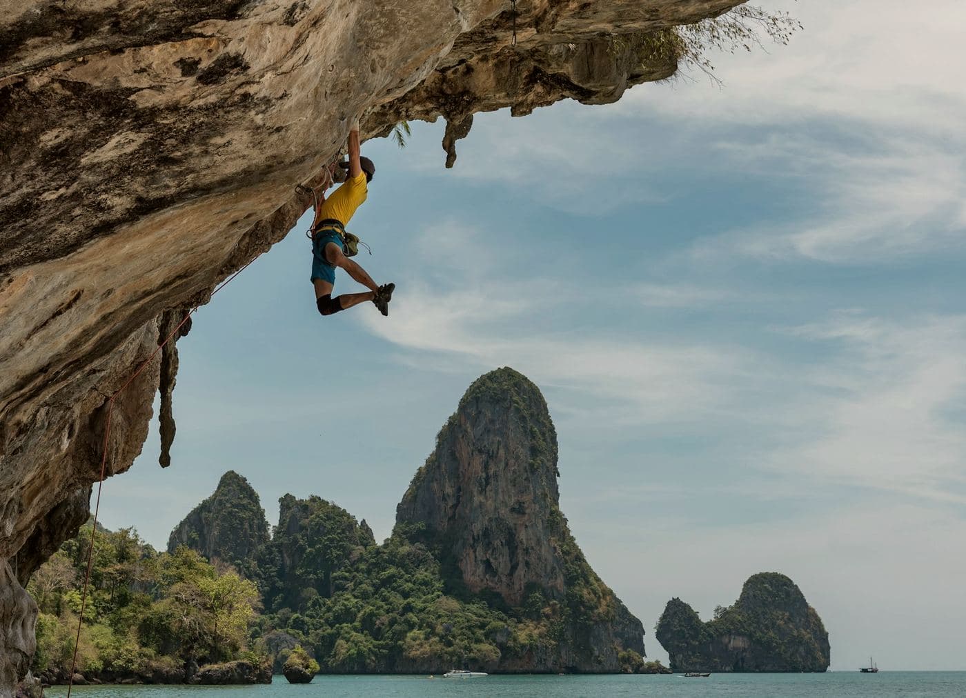 A climber part-way up an overhang, open water and limestone stacks behind.