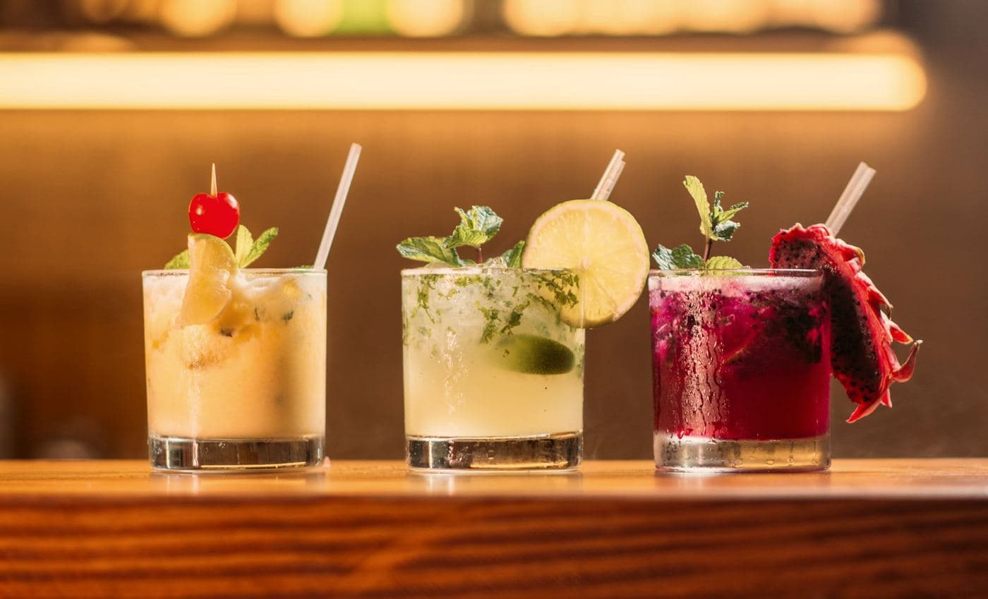 Cocktails lined up along a bar counter under a warm strip light.
