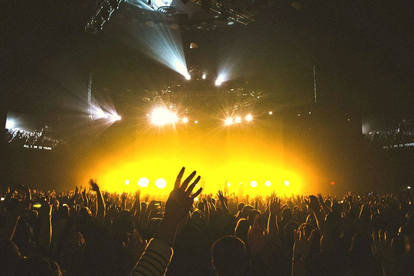 A crowd in silhouette with hands in the air, lit amber from the stage.