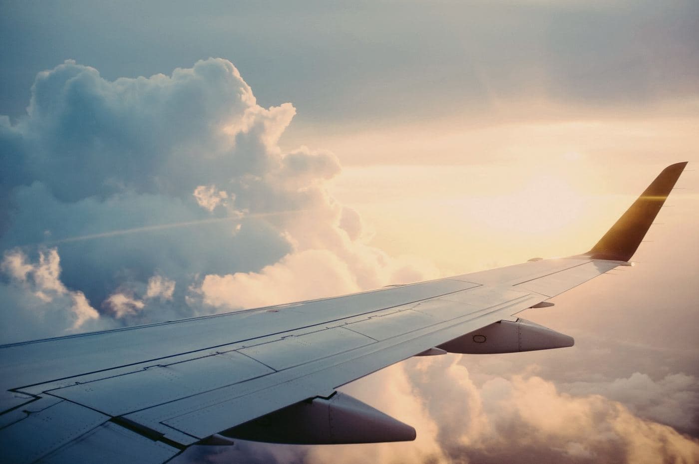 A wing out of a window seat, above cloud, in late gold light.